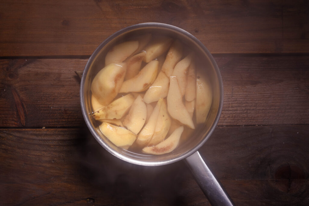 Quitten kochen mit Wasser und Rohrzucker in einem Topf.