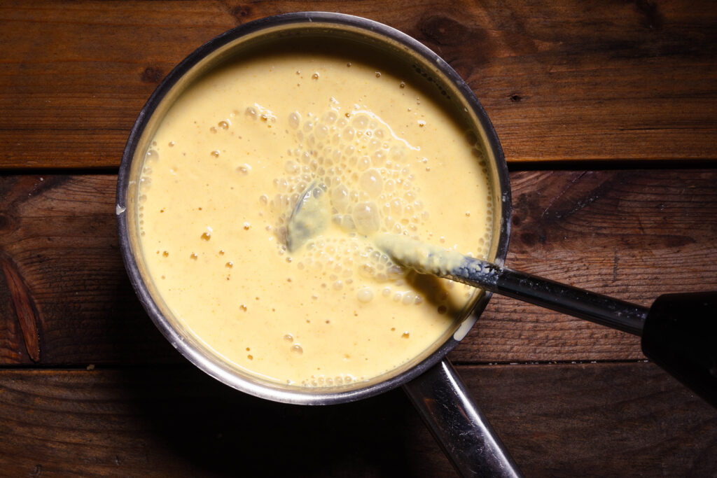 Ein Pürierstab püriert ein Joghurtgetränk in einem Topf.