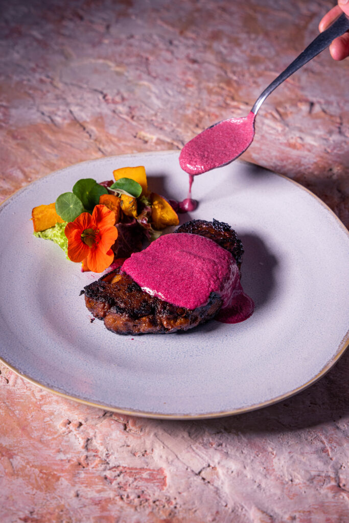 Schlehen-Gin-Sauce wird auf einen Teller mit Seitanfilet, Salat und Kürbis angerichtet.