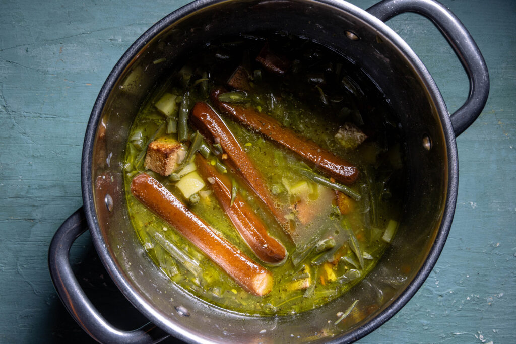 Schnippelbohnensuppe mit Würsten gart in einem Kochtopf.