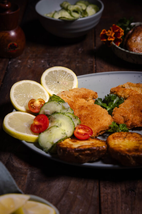 Steinpilz-Schnitzel - frisch aus dem Wald und vegan, auf einem Teller mit Zitrone, Gurkensalat und gerösteten Kartoffeln.
