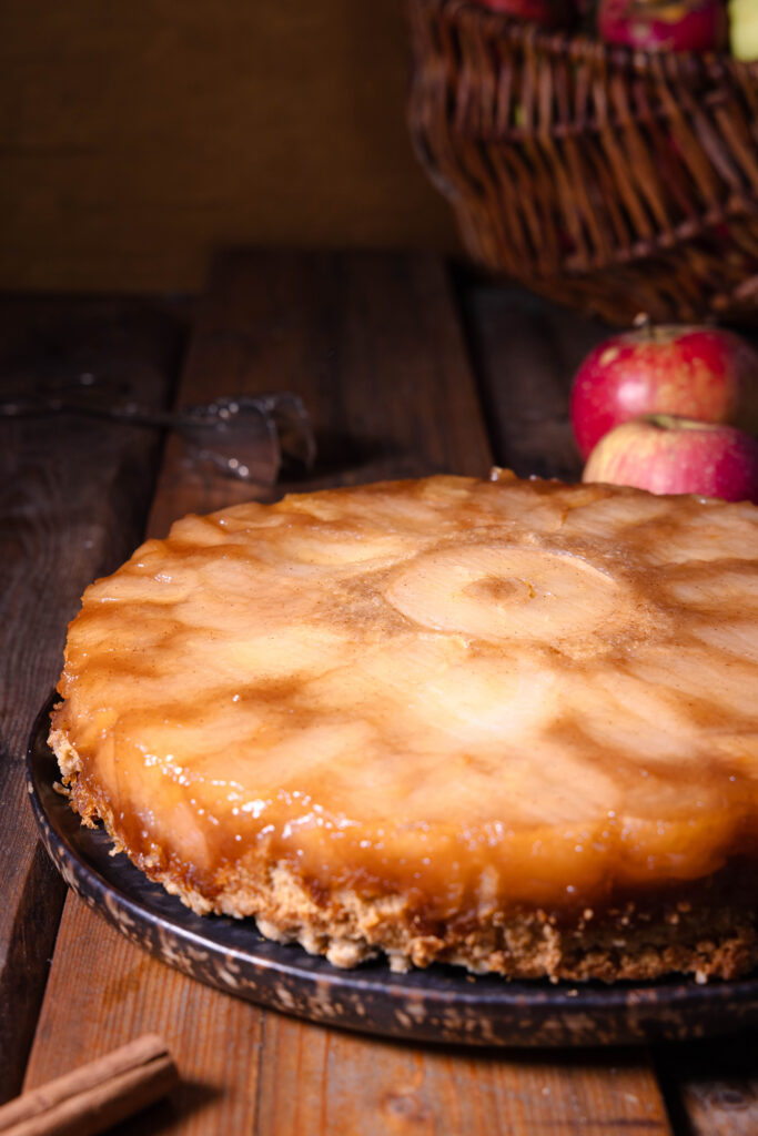 Überkopf-Apfelkuchen mit der Fruchtschicht nach oben. Dahinter frische, rote Äpfel.