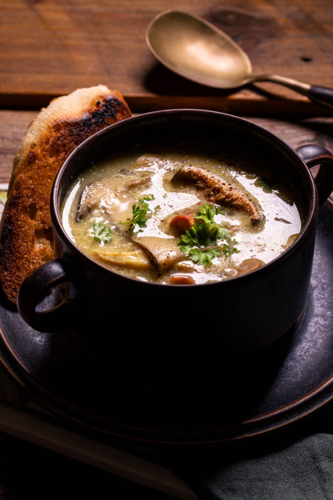 Eine Schüssel mit Waldpilzsuppe. Außerdem ein Löffel und geröstetes Brot.