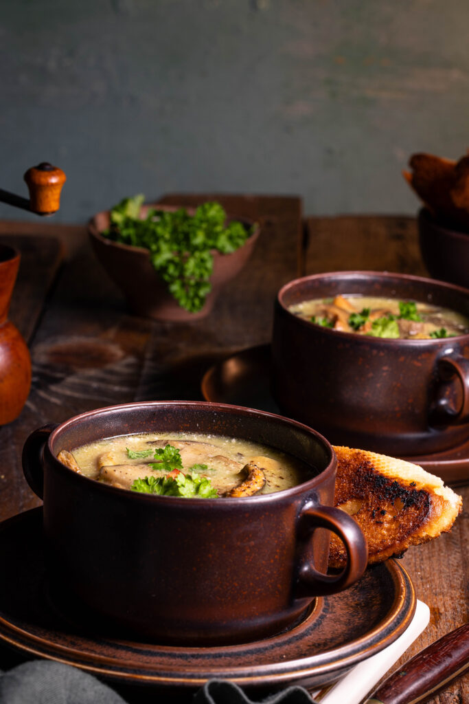Zwei Schüsseln mit Waldpilzsuppe. Außerdem ein Löffel und geröstetes Brot.