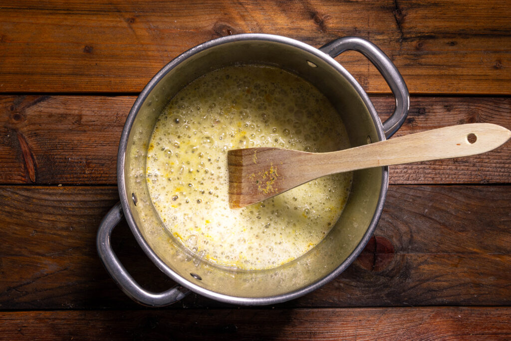 Ein Topf mit blubbernder veganer Butter und Schalottenwürfeln darin.