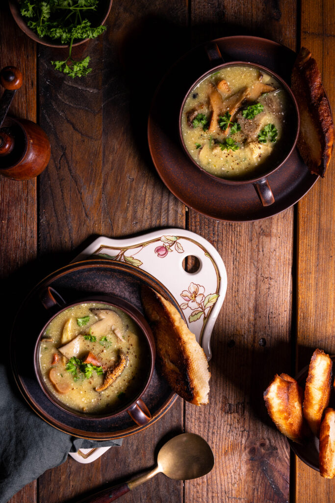 Zwei Schalen mit Waldpilzsuppe. Außerdem Brot und Kräuter.
