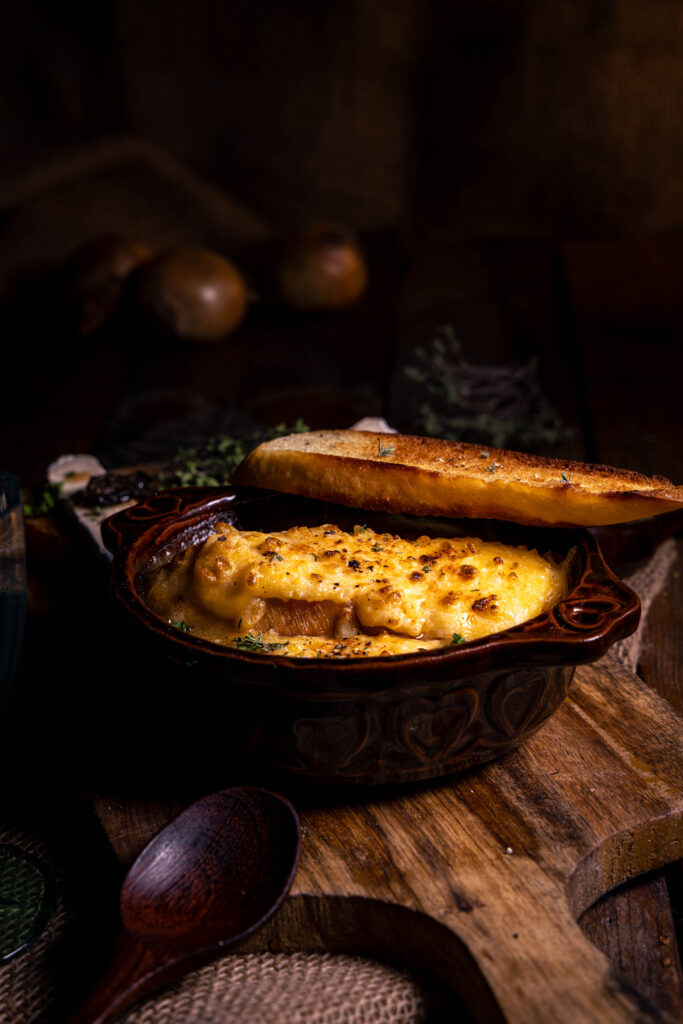 Soupe à l'oignon. In einer feuerfesten, braunen Schale, darauf eine Extrascheibe geröstetes Brot.