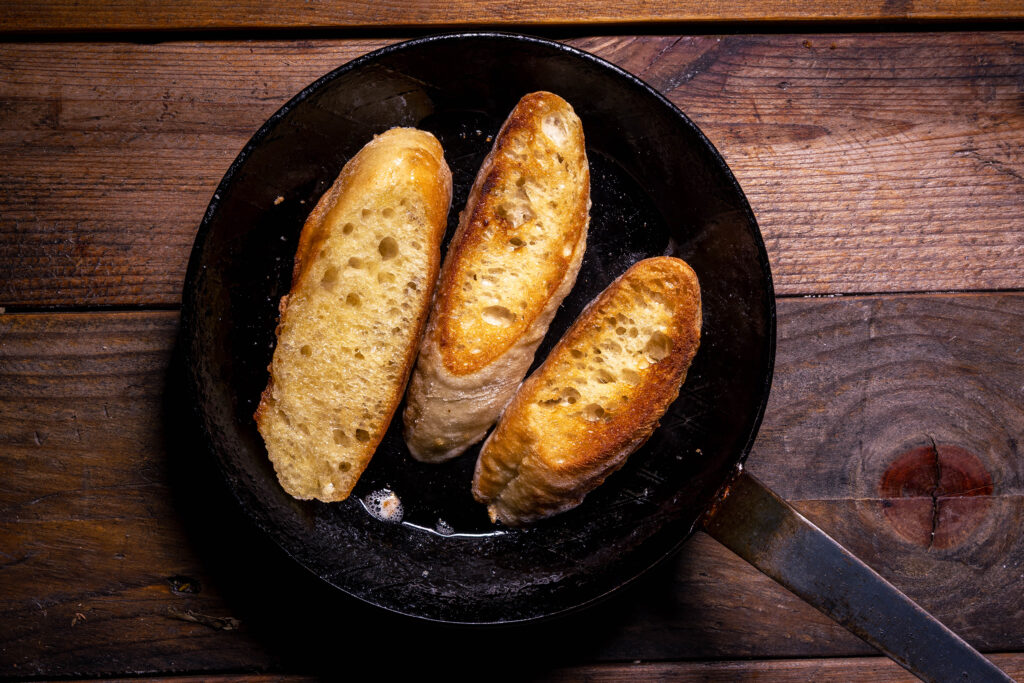 3 Baguttescheiben werden in einer Pfanne geröstet.