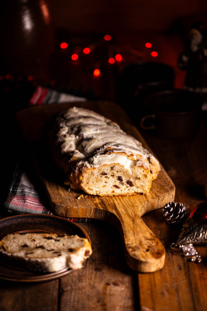 Veganer Weihnachtsstollen, angeschnitten auf einem Holzbrett, ein Stück auf einem Teller, darum Weihanchtsdeko.