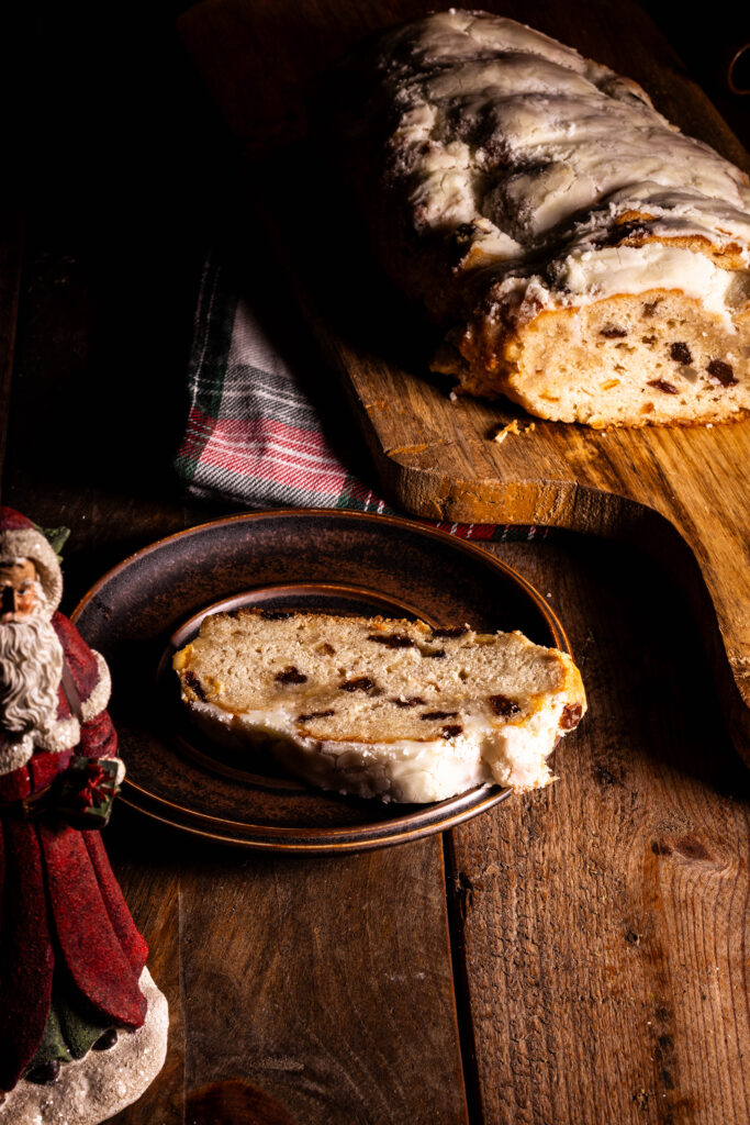 Veganer Christstollen - Dresdner Stollen rein pflanzlich, angeschnitten auf einem Holzbrett, ein Stück auf einem Teller. Davor ein kleiner Weihnachtsmann.