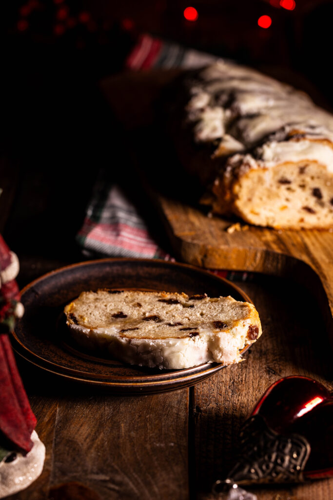 Veganer Christstollen angeschnitten auf einem Holzbrett, eine Scheibe auf einem Teller. Darum: antike Weihnachtsdeko
