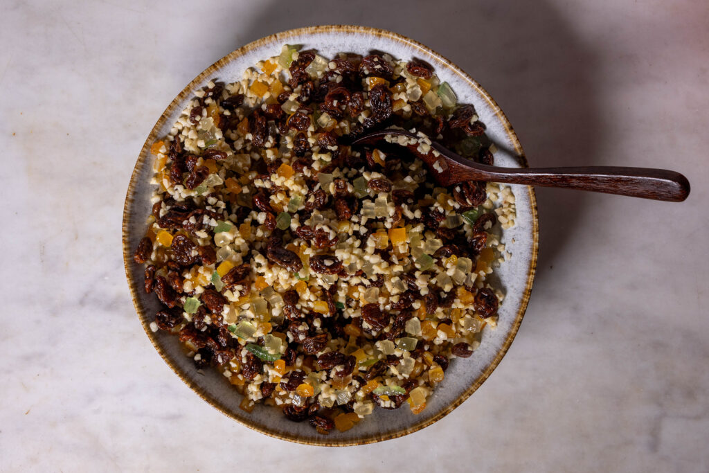 Zitronenabrieb, Orangeat, Zitronat und gehackte Mandeln zusammen mit Rum und Rosinen in einer Schale.
