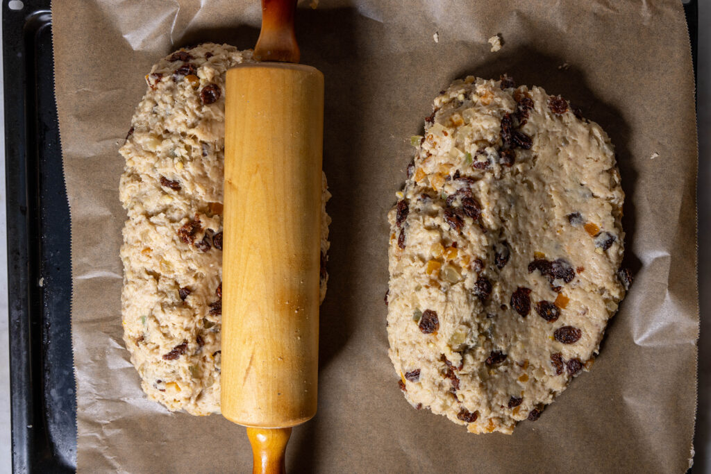 Zwei Laibe Stollenteig. Mit der Teigrolle wird etwa die Hälfte des Stollens über die lange Kante etwas flach abgerollt.
