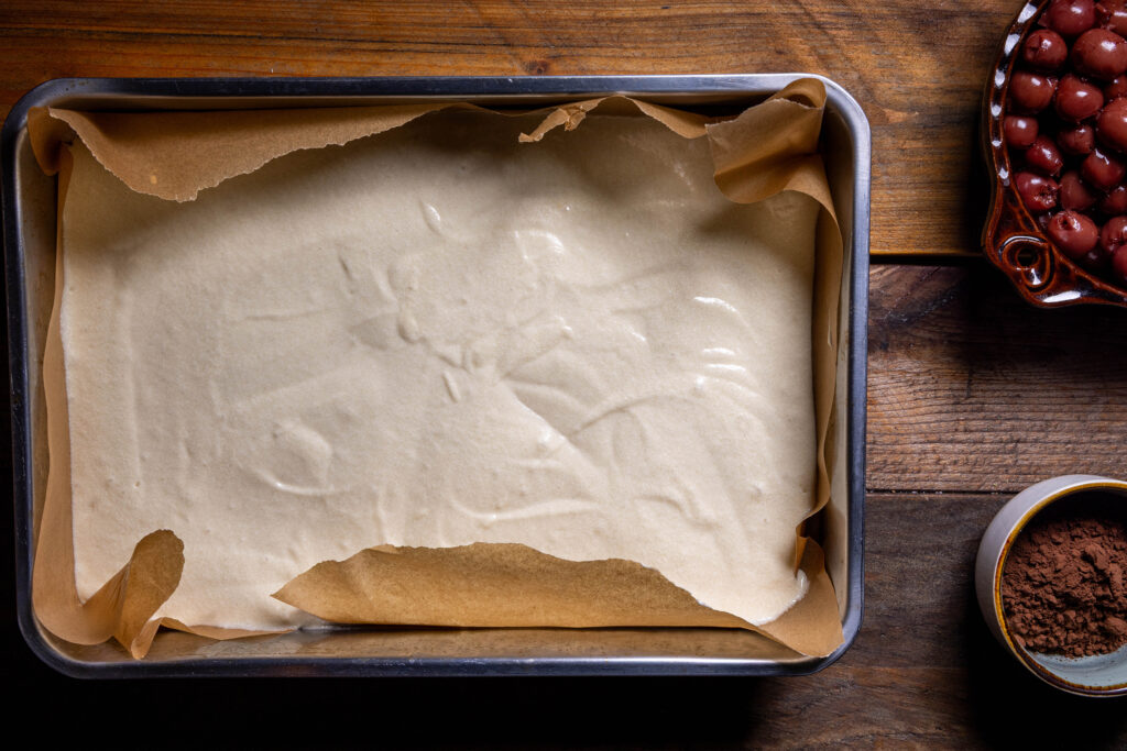 Ein mittelgroßes Backblech mit Backpapier ausgelegt und Kuchenteig darin.