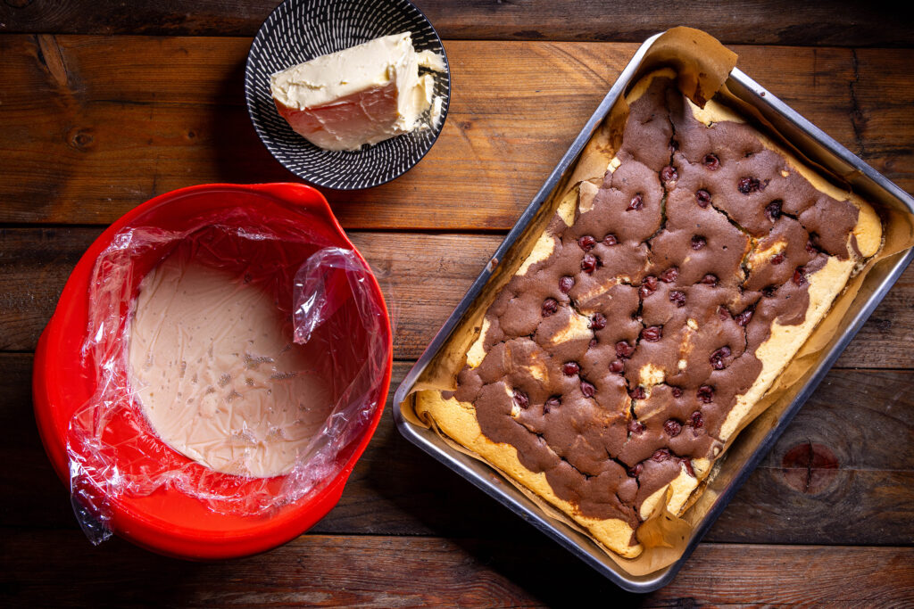 Eine Rührschüssel mit mit Folie abgeddecktem Pudding und ein gebackener Donauwellenboden.