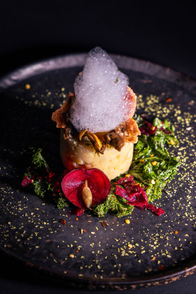 Geräuchertes Topinambur-Quitten-Püree mit Minzschaum, Trompetenpfifferlingen, Grünkohl und Beete angerichtet.