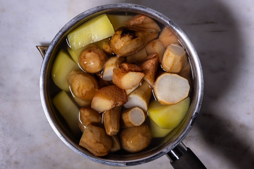 Kartoffeln, geräucherte Quitten und geräucherter Topinambur kochen in Salzwasser in einem Topf.