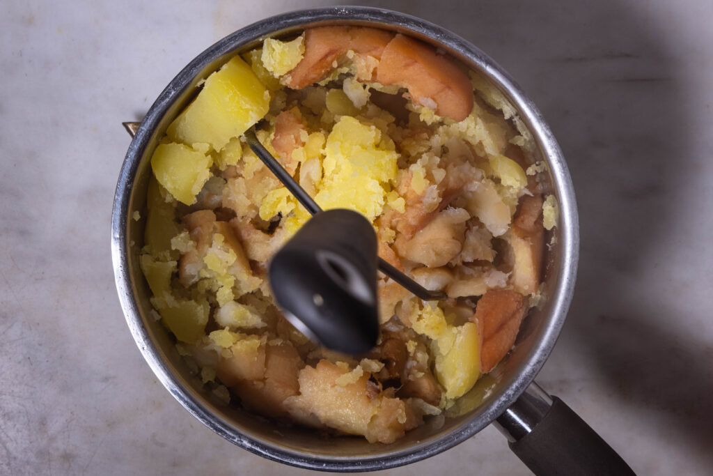 Ein Püree wird in einem Topf gestampft.