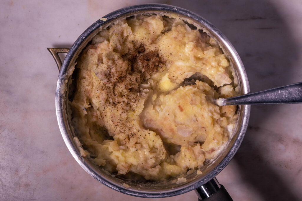 Geräuchertes Topinambur-Quitten-Püree wird in einem Kochtopf mit Gewürzen verrührt.