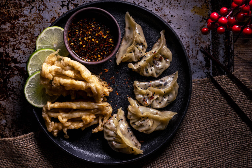Vegane Gyoza mit Dip, Limette und frittierten Pilzen auf einem Teller.