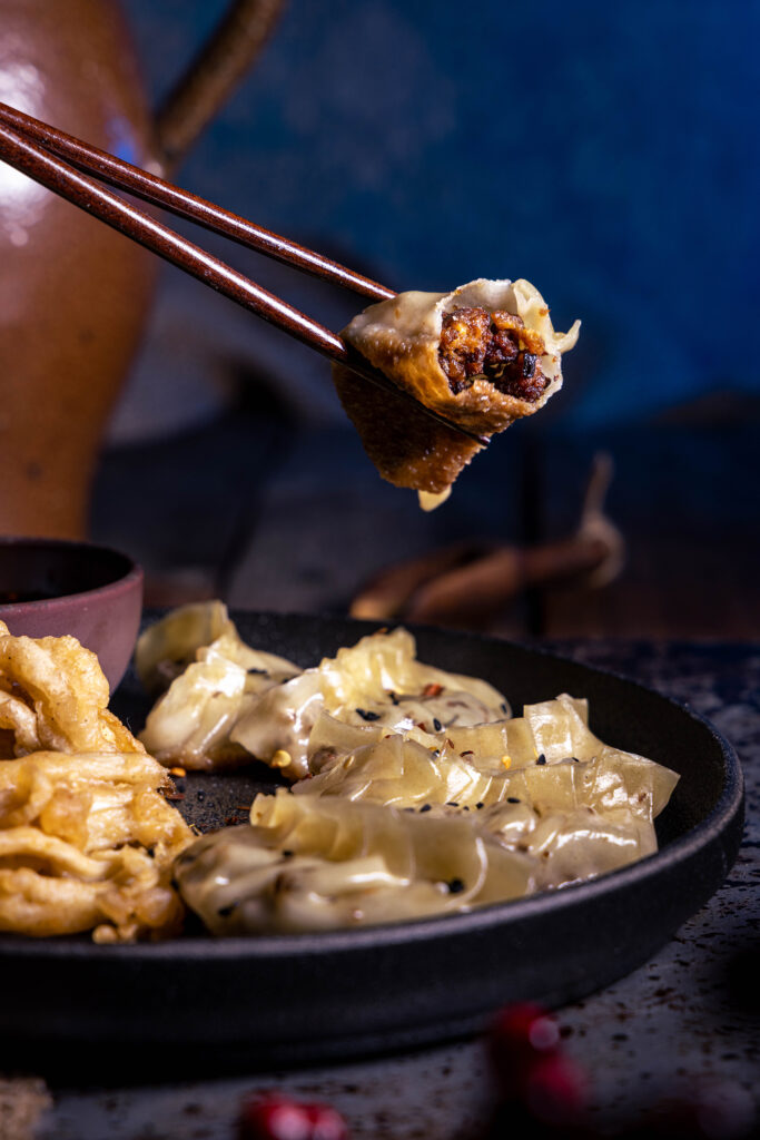 Vegane Gyoza: auf einem Teller und angebissen zischen Stäbchen.
