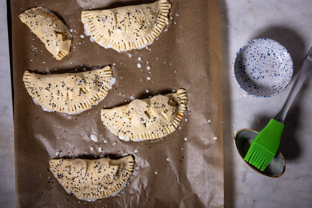 Mit Sesam und Schwarzkümmel bestreute Teigtaschen auf einem Backblech.