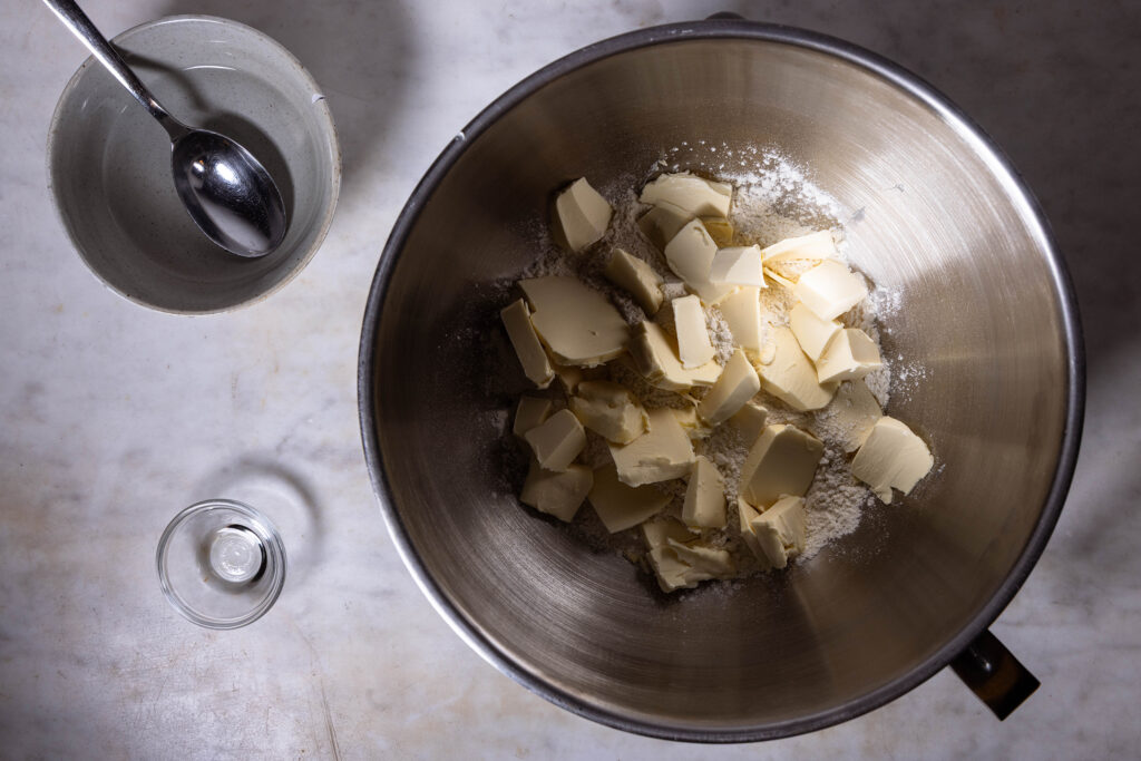 Veganer Mürbeteig wird zubereitet. Kalte vegane Butterstücke in einer Schüssel mit Mehl.