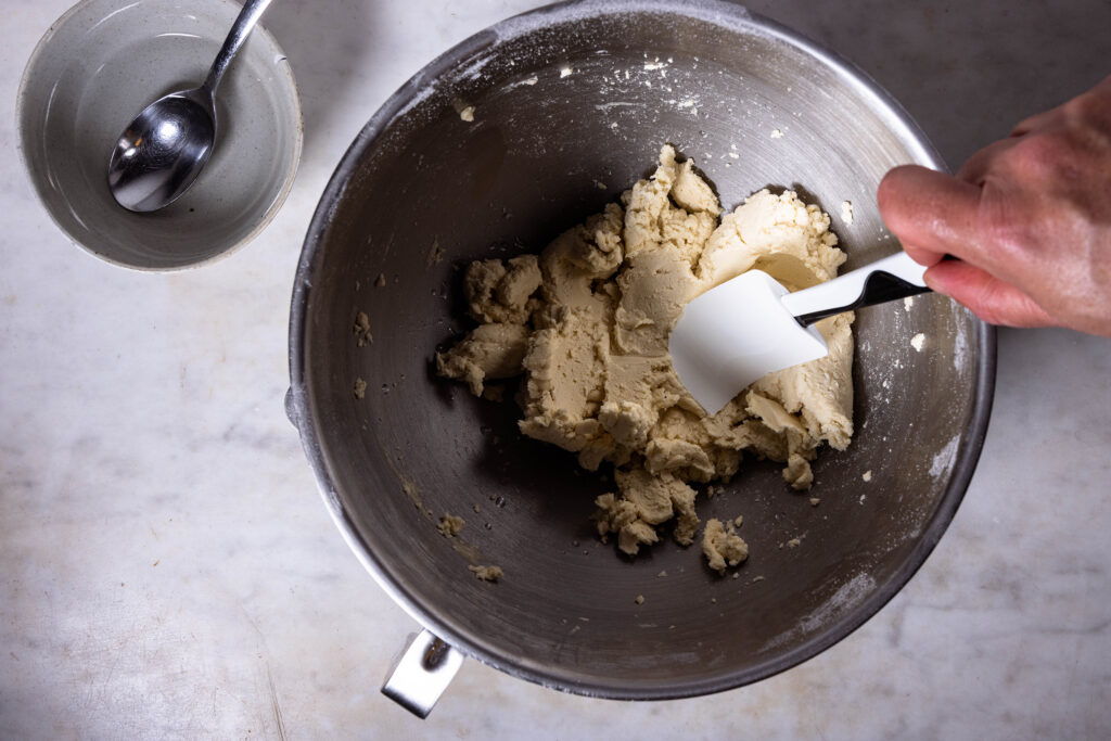 Veganer Mürbeteig wird zubereitet. Kaltes Wasser wird mit einem Küchensapchtel in den Teig eingearbeitet.