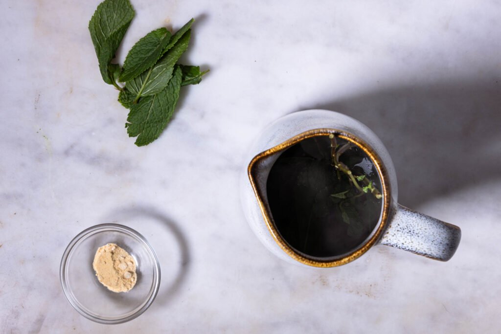 Minztee zeiht in einer kleinen Karaffe. Daneben weitere Zutaten.