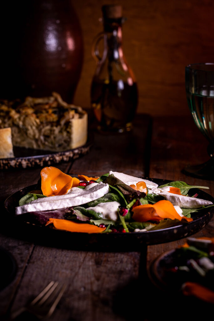 Orangebecherling-Salat - frisch und farbenfroh auf zwei Tellern. Dahinter eine Waldpilz-Wirsing-Quiche und eine Flasche Olivenöl.
