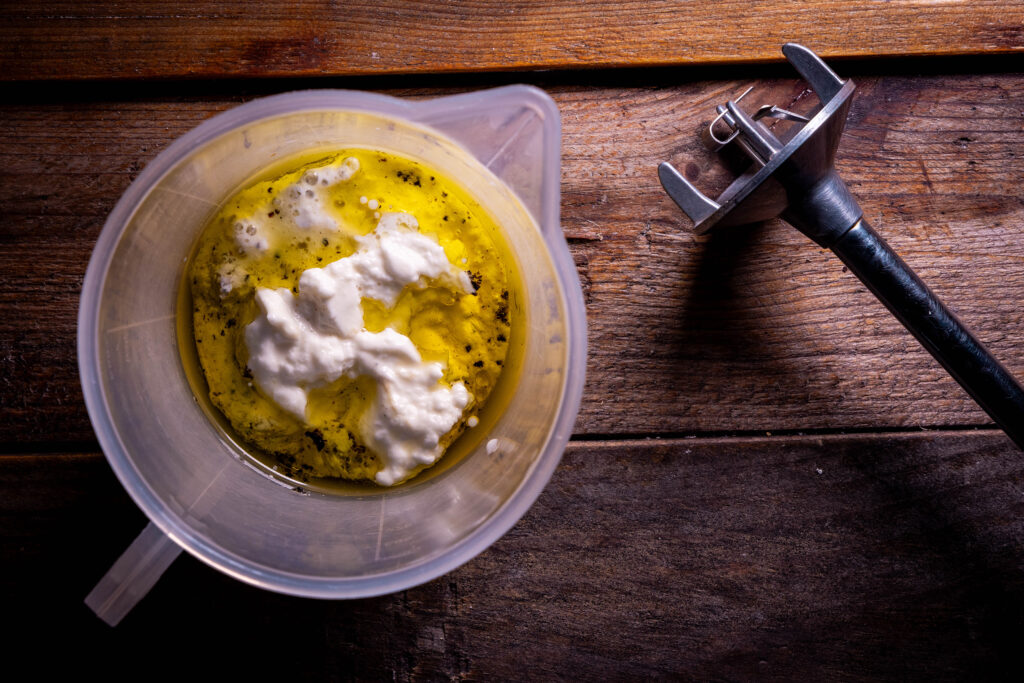 Dressingzutaten in einem Messbecher und ein Pürierstab.