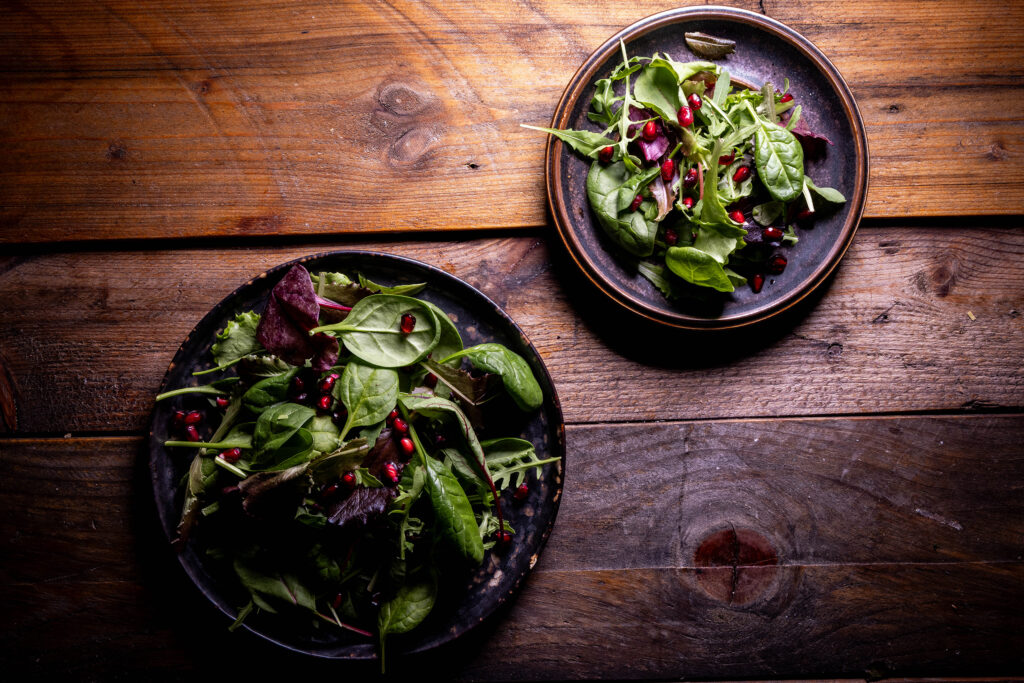 2 Salatteller mit Spinat, Salatblättern und Granatapfelkernen.