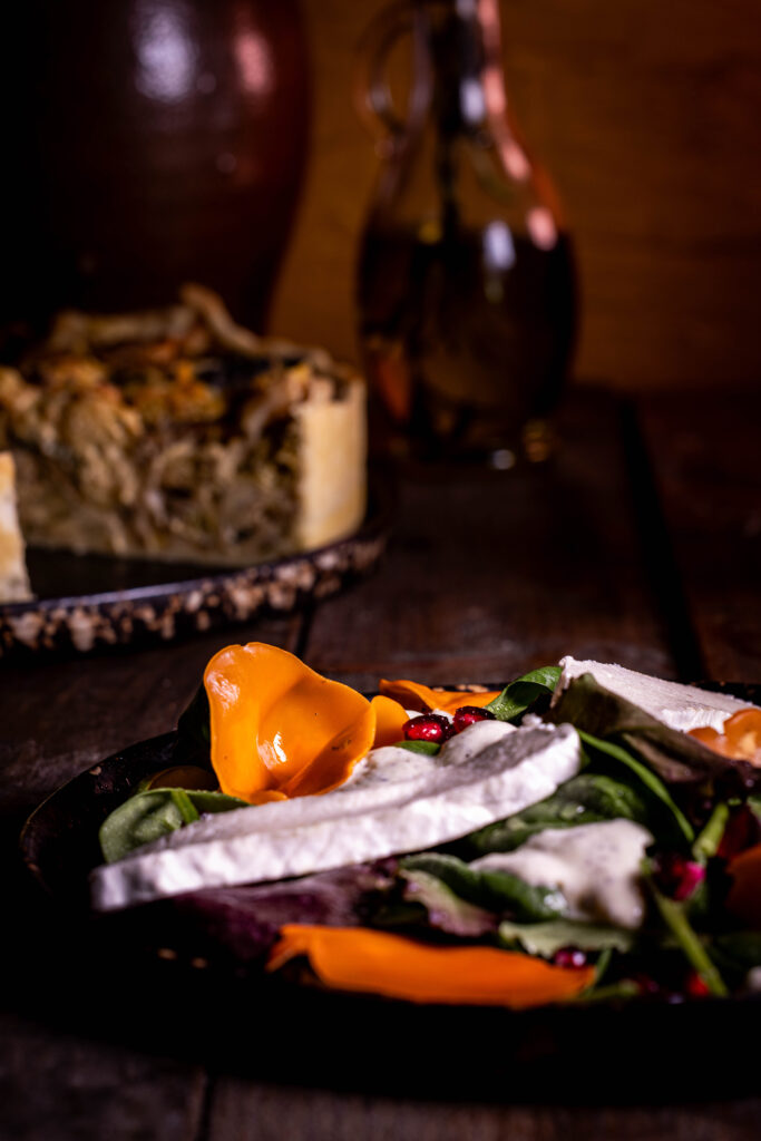Orangebecherling-Salat - frisch und farbenfroh auf zwei Tellern. Dahinter eine Waldpilz-Wirsing-Quiche und eine Flasche Olivenöl.