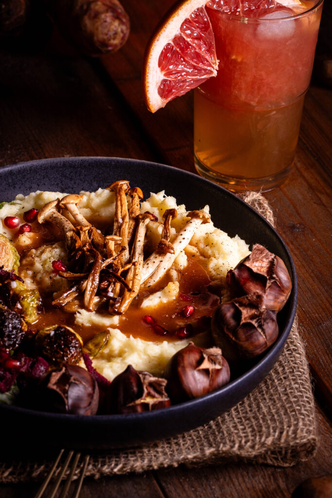 Pastinakenpüree mit gerösteten Maronen, gebratenen Pilzen, geröstetem Rosenkohl und Bratensauce auf einem Teller.