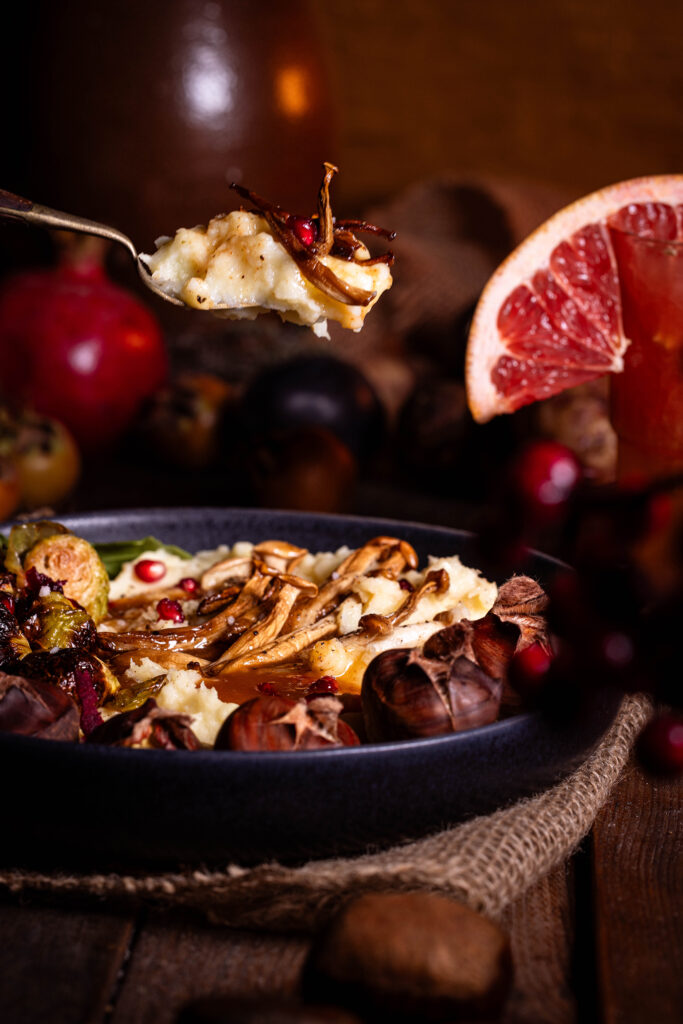 Pastinakenpüree mit gerösteten Maronen, gebratenen Pilzen, geröstetem Rosenkohl und Bratensauce auf einem Teller.