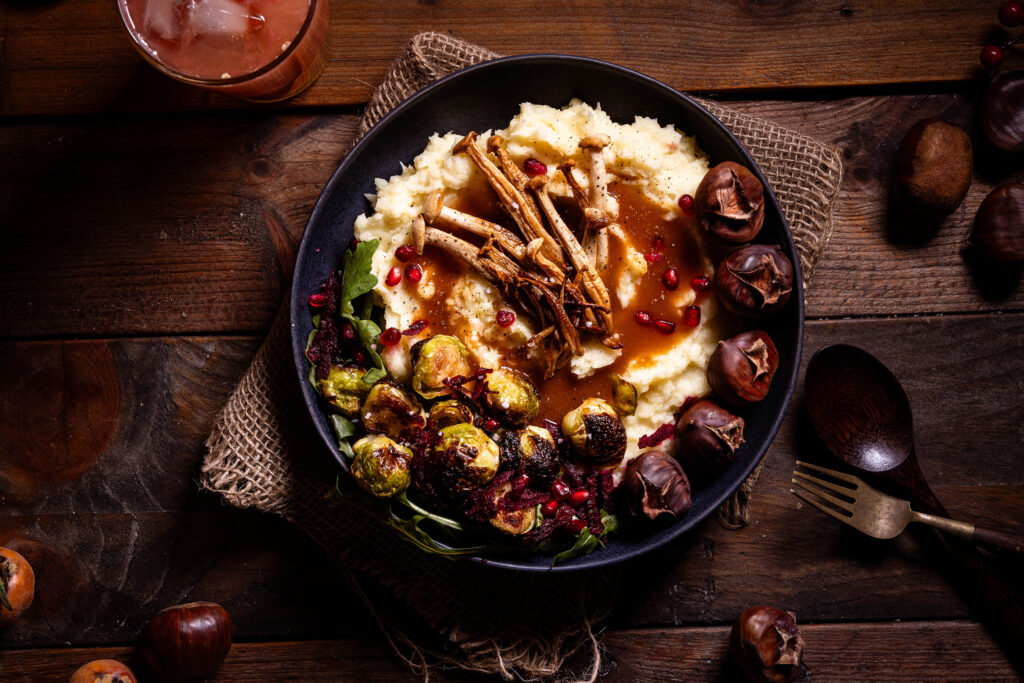 Pastinakenpüree mit gerösteten Maronen, gebratenen Pilzen, geröstetem Rosenkohl und Bratensauce auf einem Teller.