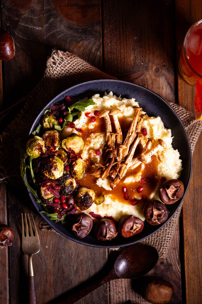 Pastinakenpüree mit gerösteten Maronen, gebratenen Pilzen, geröstetem Rosenkohl und Bratensauce auf einem Teller.