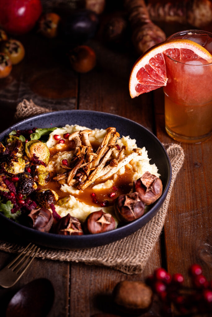 Pastinakenpüree mit gerösteten Maronen, gebratenen Pilzen, geröstetem Rosenkohl und Bratensauce auf einem Teller.