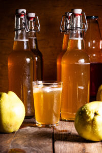 Quitten-Kombucha – als fruchtige Zweitfermentation, in Flaschen und in einem Glas. Außerdem 2 frische Quitten.