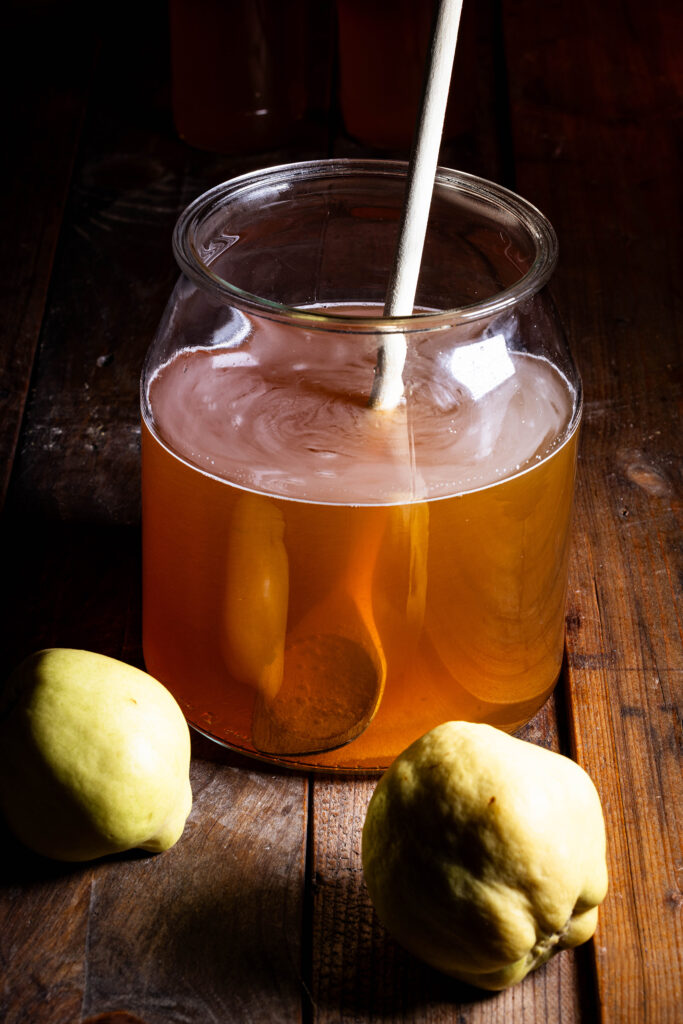 Rohrzucker wird in ein Gefäß mit Kombucha eingerührt.