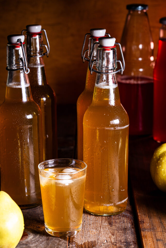 Quitten-Kombucha im Glas, dahinter Flaschen