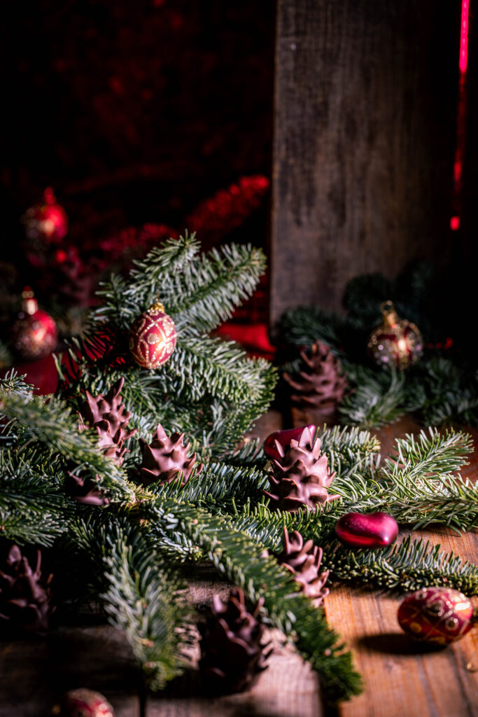 Schokozapfen - Marzipan-Tannenzapfen - dekorativ mit Weihnachtsbaumschmuck in Tannenzweigen platziert.