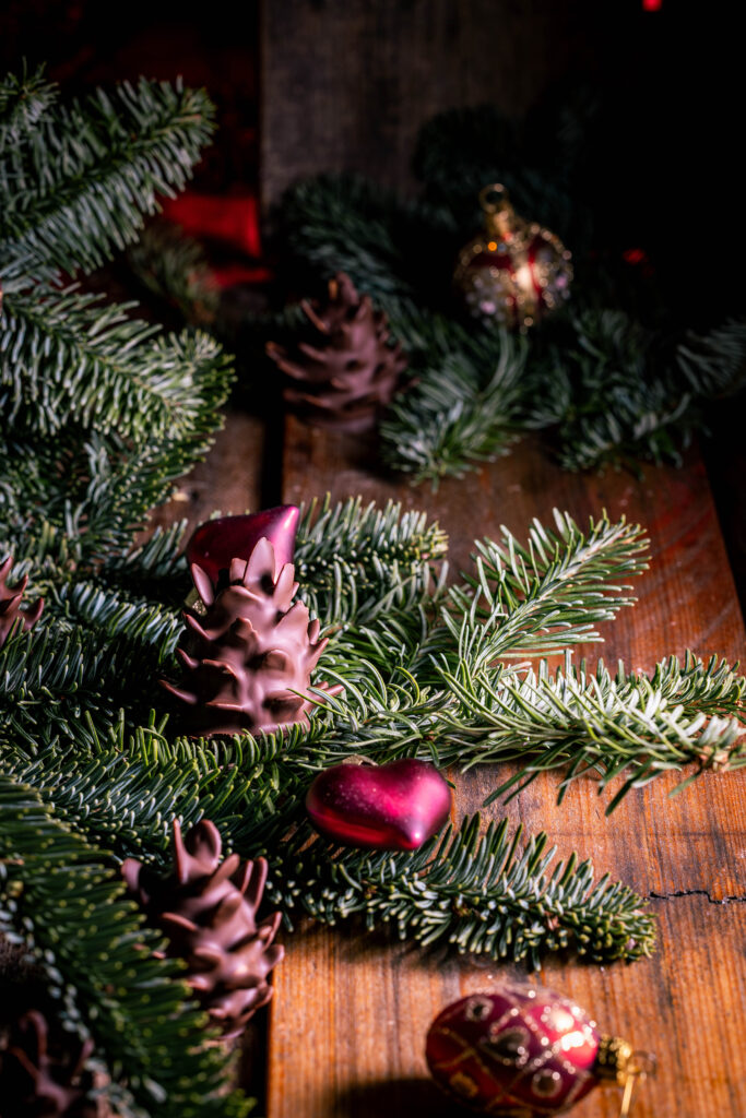 Schokozapfen - Marzipan-Tannenzapfen - dekorativ mit Weihnachtsbaumschmuck in Tannenzweigen platziert.
