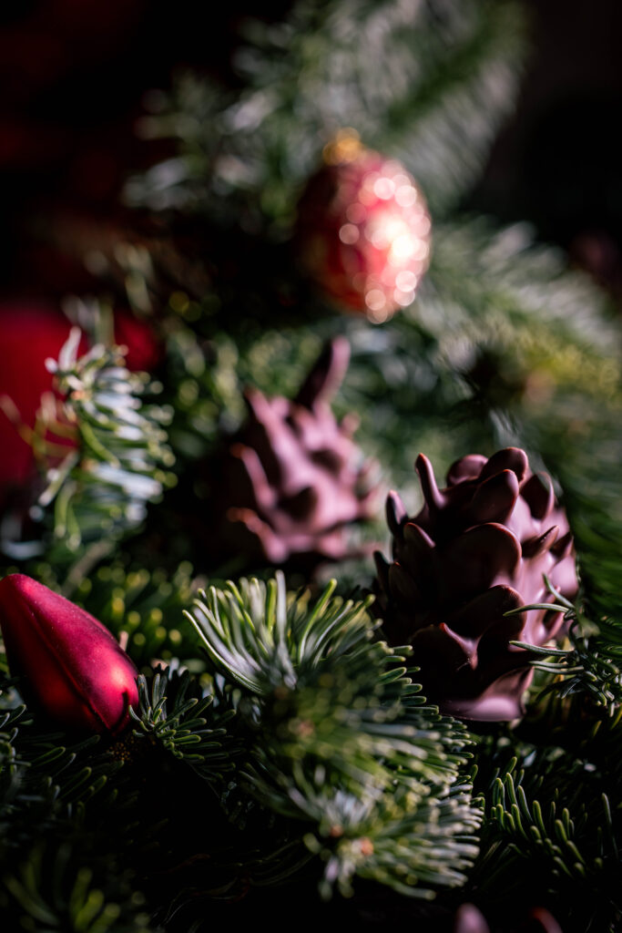 Schokozapfen - Marzipan-Tannenzapfen - dekorativ mit Weihnachtsbaumschmuck in Tannenzweigen platziert.