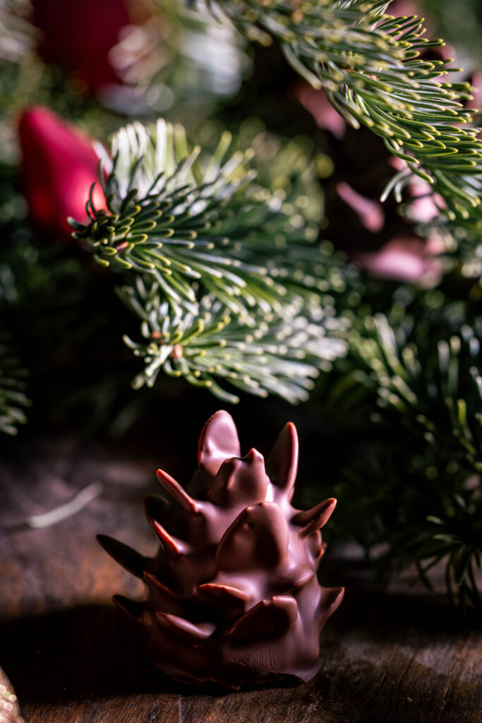 Schokozapfen - Marzipan-Tannenzapfen - dekorativ mit Weihnachtsbaumschmuck in Tannenzweigen platziert.