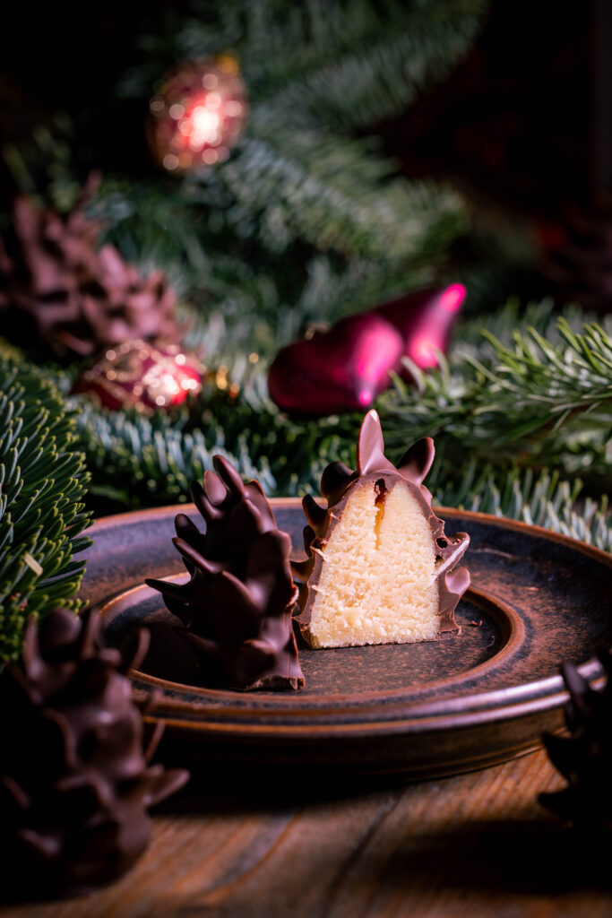 Süße Marzipan-Tannenzapfen, gespickt mit knackigen Mandelhobeln, umhüllt von zarter Schokolade. Angeschnitten auf einem Teller.