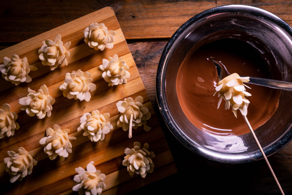 Marzipan-Mandel-Zapfen, einer auf einem Holzspieß aufgespießt und eine Schale mit geschmolzener Kuvertüre.