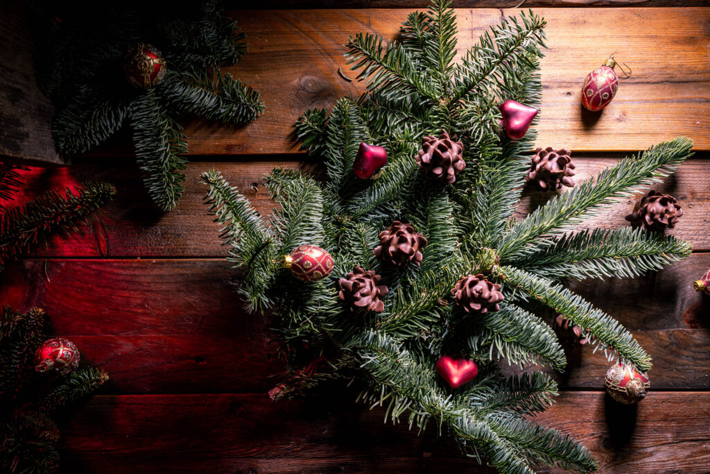 Schokozapfen - Marzipan-Tannenzapfen - dekorativ mit Weihnachtsbaumschmuck in Tannenzweigen platziert.