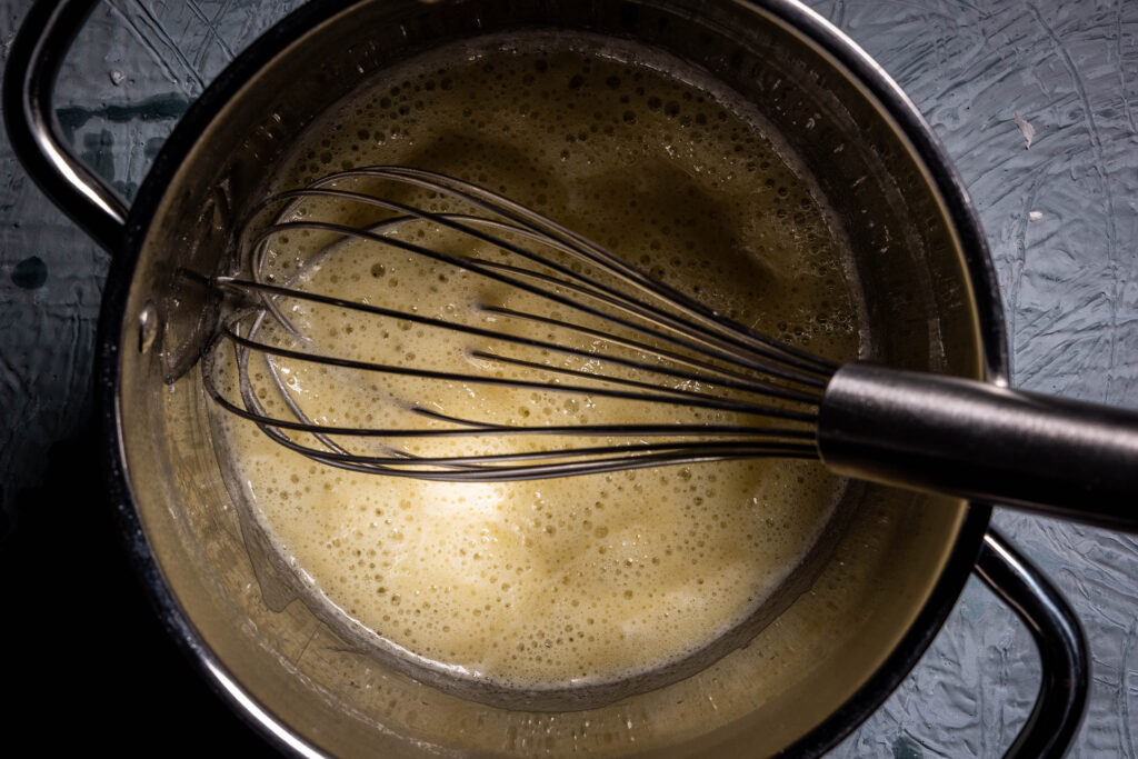 Vegane Mehlschwitze mit einem Schneebesen in einem Topf.