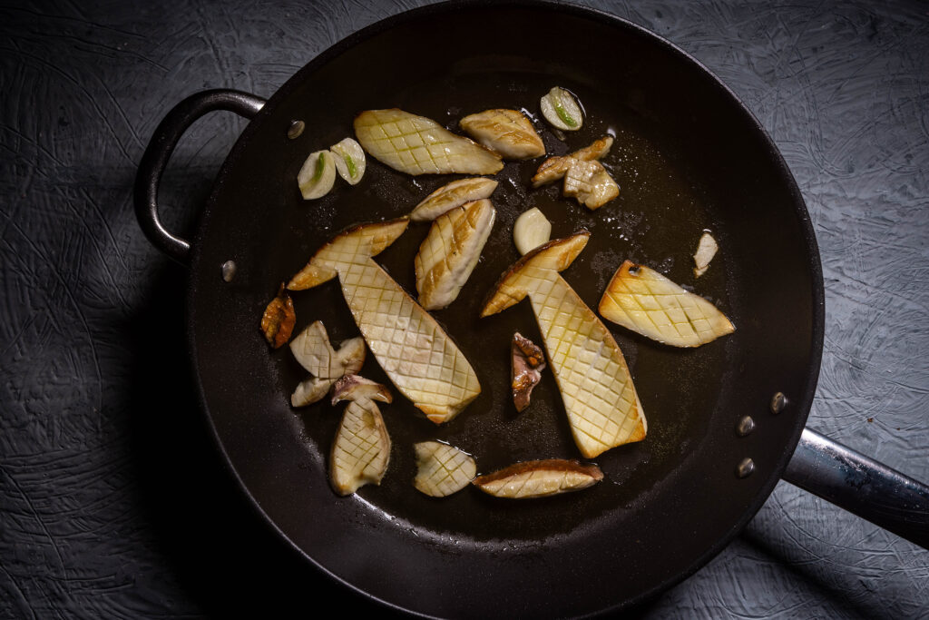 Steinpilze braten mit Knoblauch in einer Pfanne.